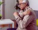 Older man holding shoulder in pain at home with marijuana leaf, Texas medical cannabis support for chronic pain.